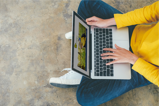 Person im gelben Pullover sitzt mit Laptop auf dem Boden. Newsletter anmelden